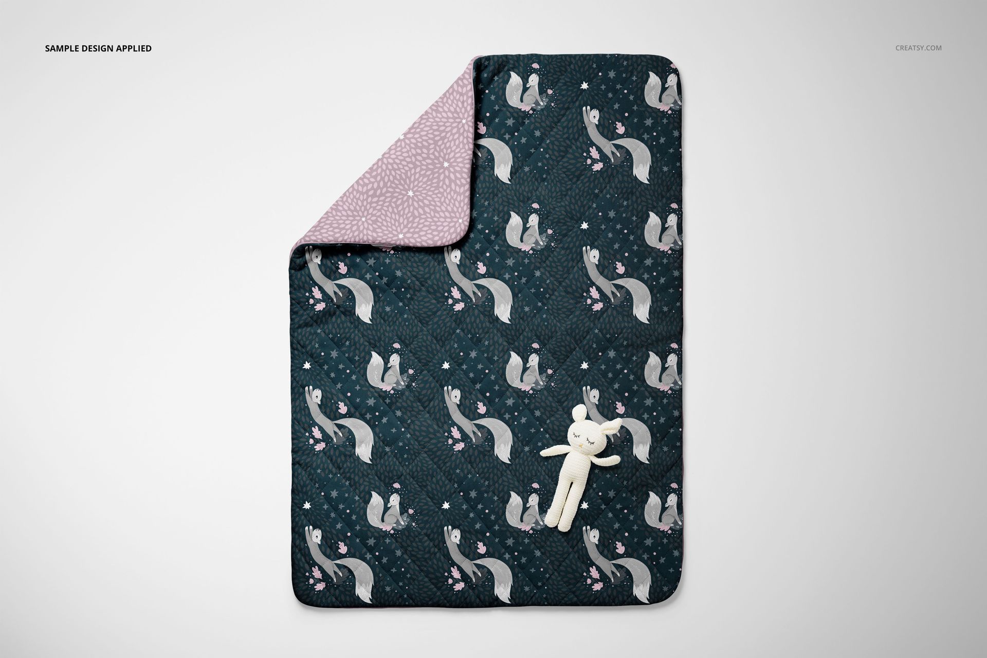 Top view of a double-sided baby bedding set mockup with a quilt and pillow in dark and pastel colors, toy included.