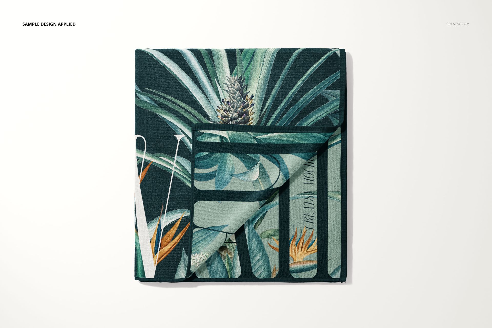 Folded beach towel mockup with tropical leaf and pineapple pattern, displayed on a light background, top view.