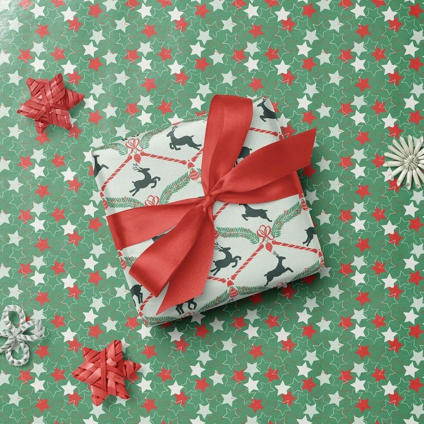 Square gift box mockup with white paper featuring black reindeer and red ribbon, placed on green star-patterned wrapping paper.