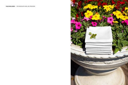 PSD mockup showing neatly folded white fabrics resting on a floral stone planter with bright summer blossoms.