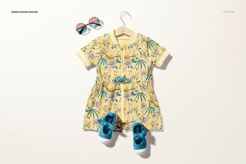 Front view of a baby dress mockup with a yellow tropical pattern, displayed on a hanger with blue shoes and sunglasses.