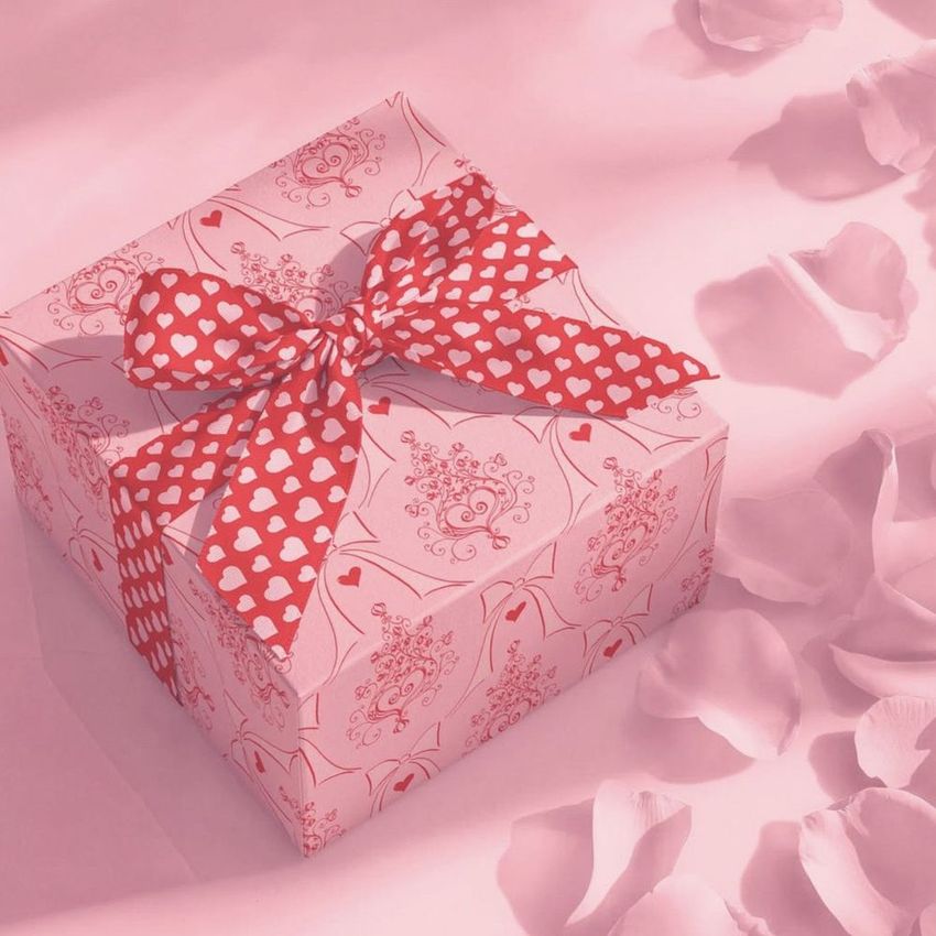 Square gift box mockup with a heart-patterned ribbon, surrounded by scattered rose petals on a soft pink background.