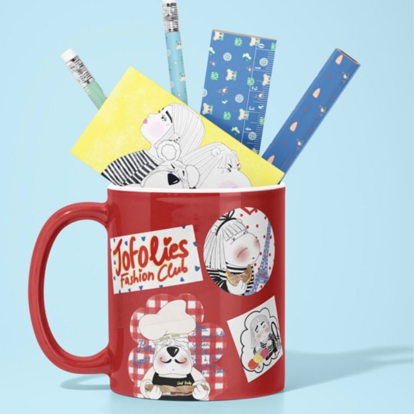 Red mug mockup decorated with illustrated stickers, holding pencils and patterned notepads, set against a light blue background.