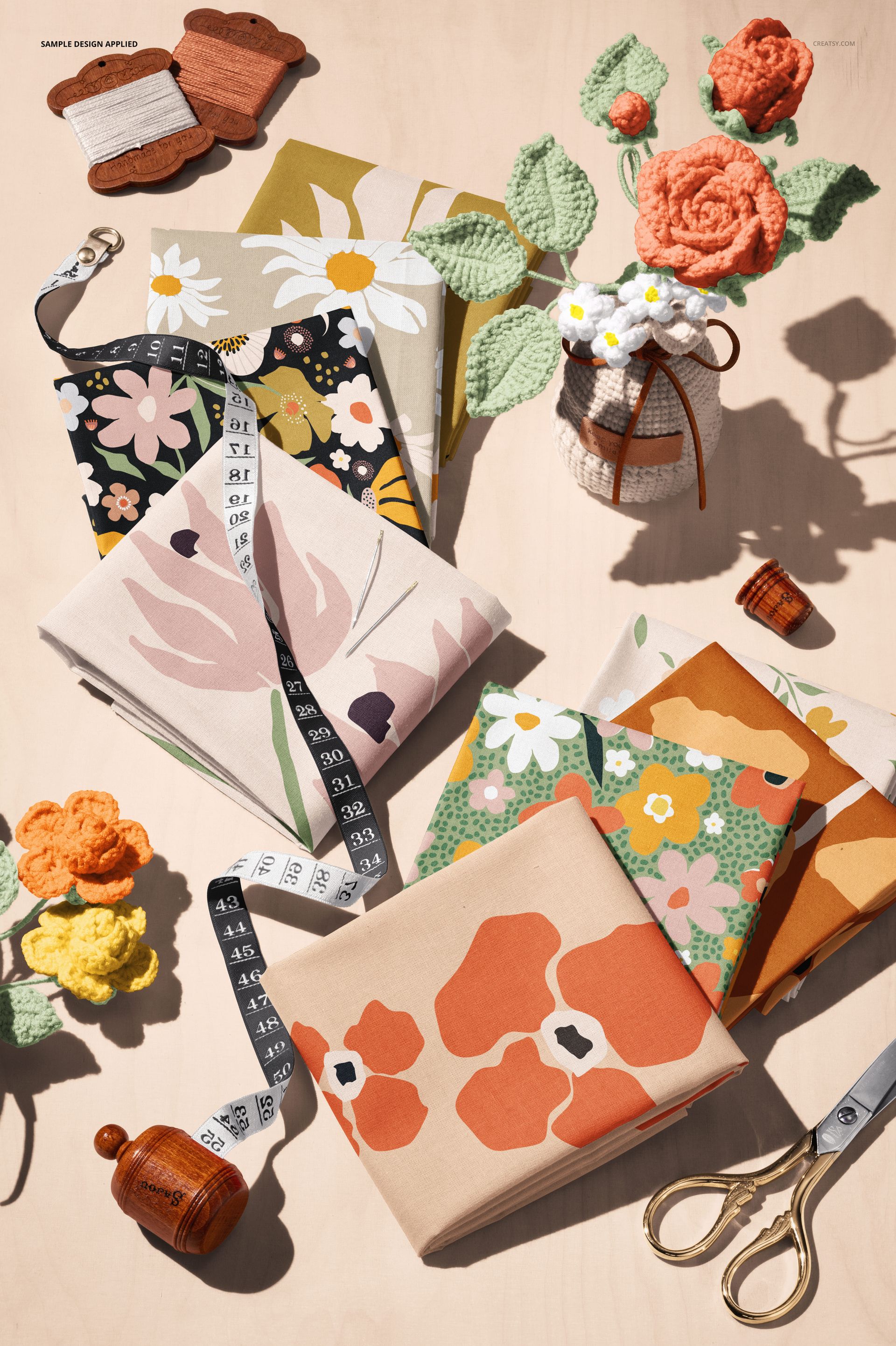 Top view of folded cotton fabric mockup featuring colorful flower prints, crocheted blooms, and measuring tape.