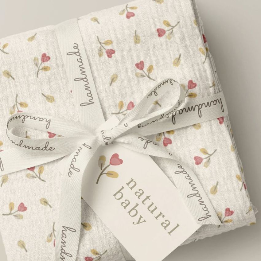 Crinkle muslin swaddle blanket mockup featuring a folded white blanket with a pink and yellow floral pattern, tied with a ribbon and tag.