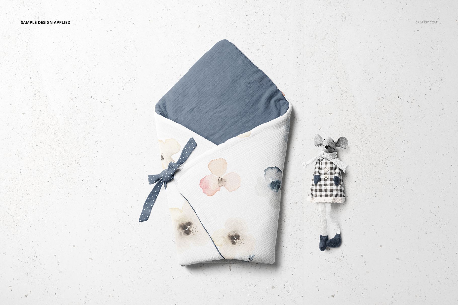 Top view of a newborn swaddle wrap mockup featuring soft blue lining and watercolor floral print, next to a plush mouse doll.