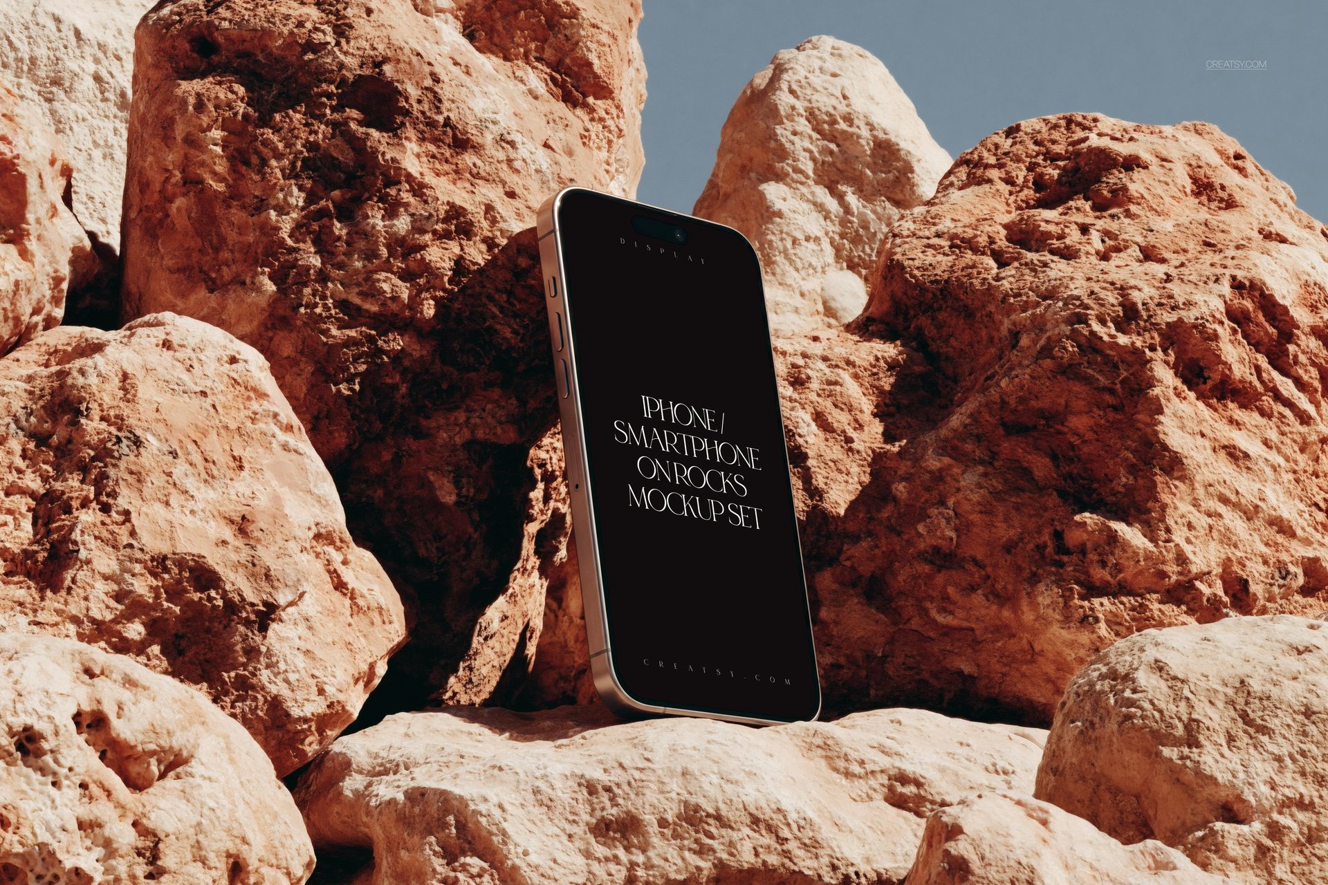 PSD mockup of an iPhone smartphone positioned vertically on rugged rocks, showing the front display clearly.