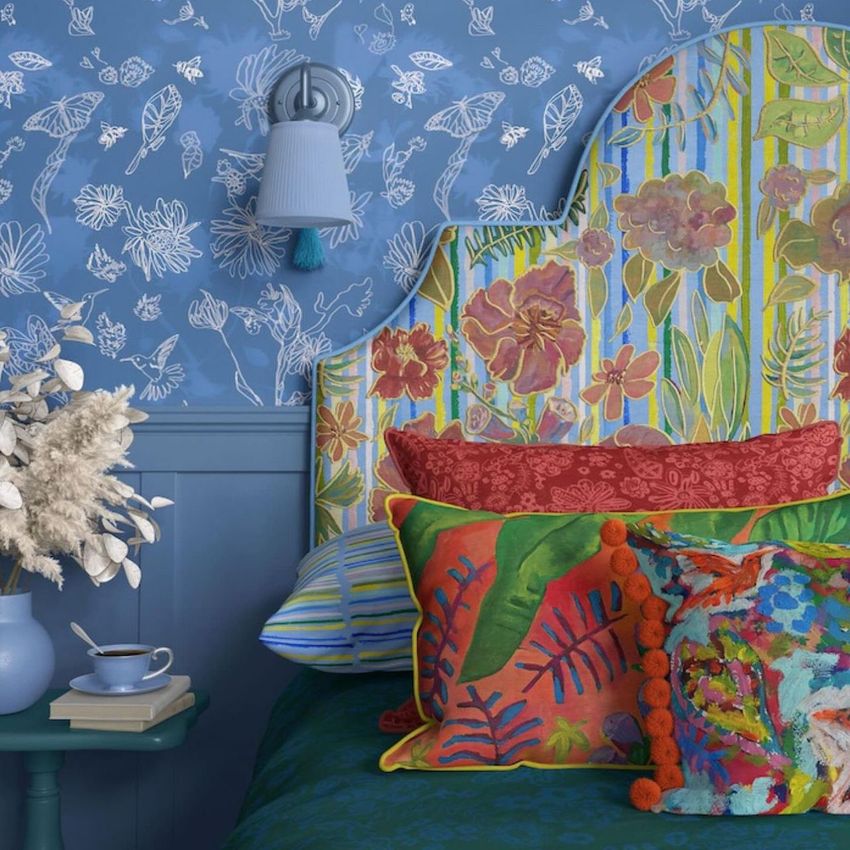 Bedroom mockup showing a colorful floral headboard, patterned pillows, and blue wallpaper with white botanical drawings.