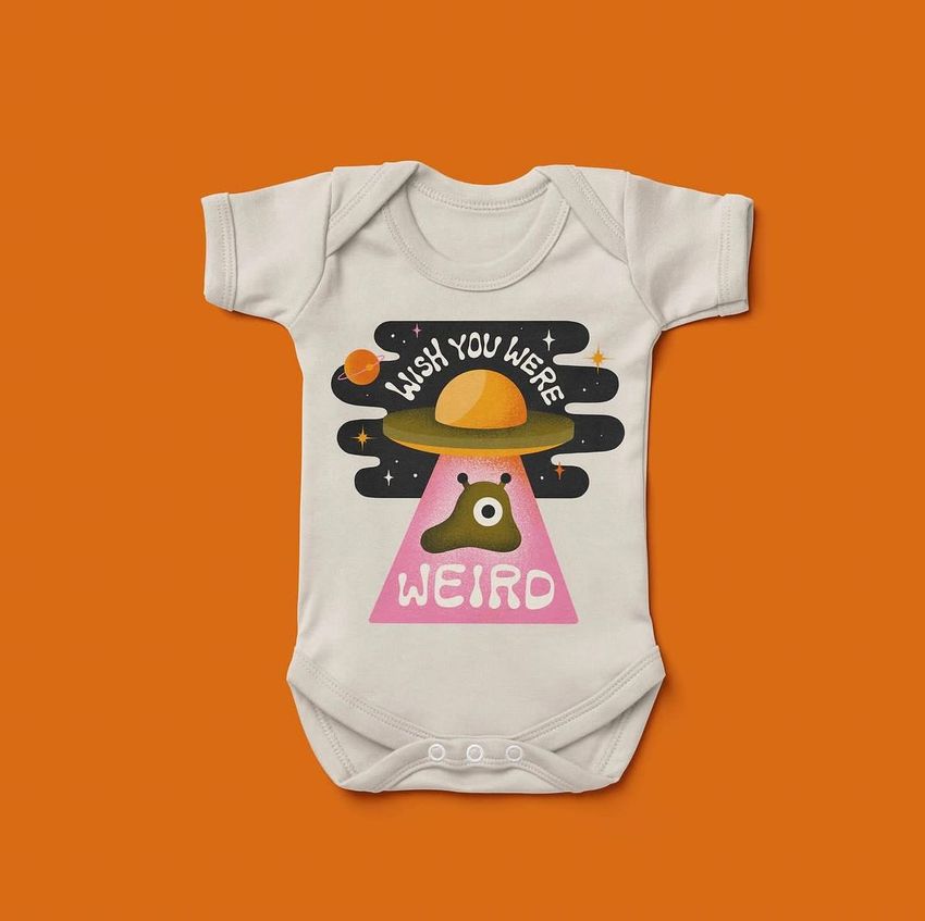 Baby short sleeve bodysuit mockup featuring a colorful alien and UFO illustration with playful text on a solid orange background.