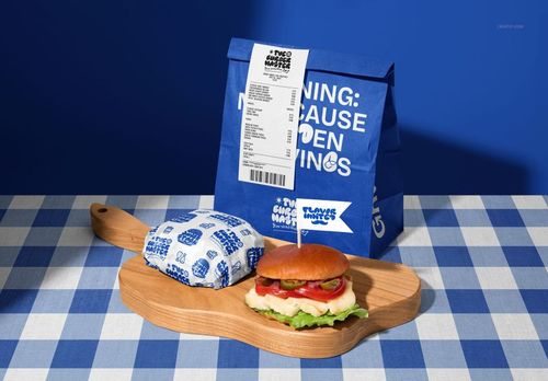 Mockup of vegan burger bar packaging, featuring a blue paper bag, wrapped burger, and wooden serving board.