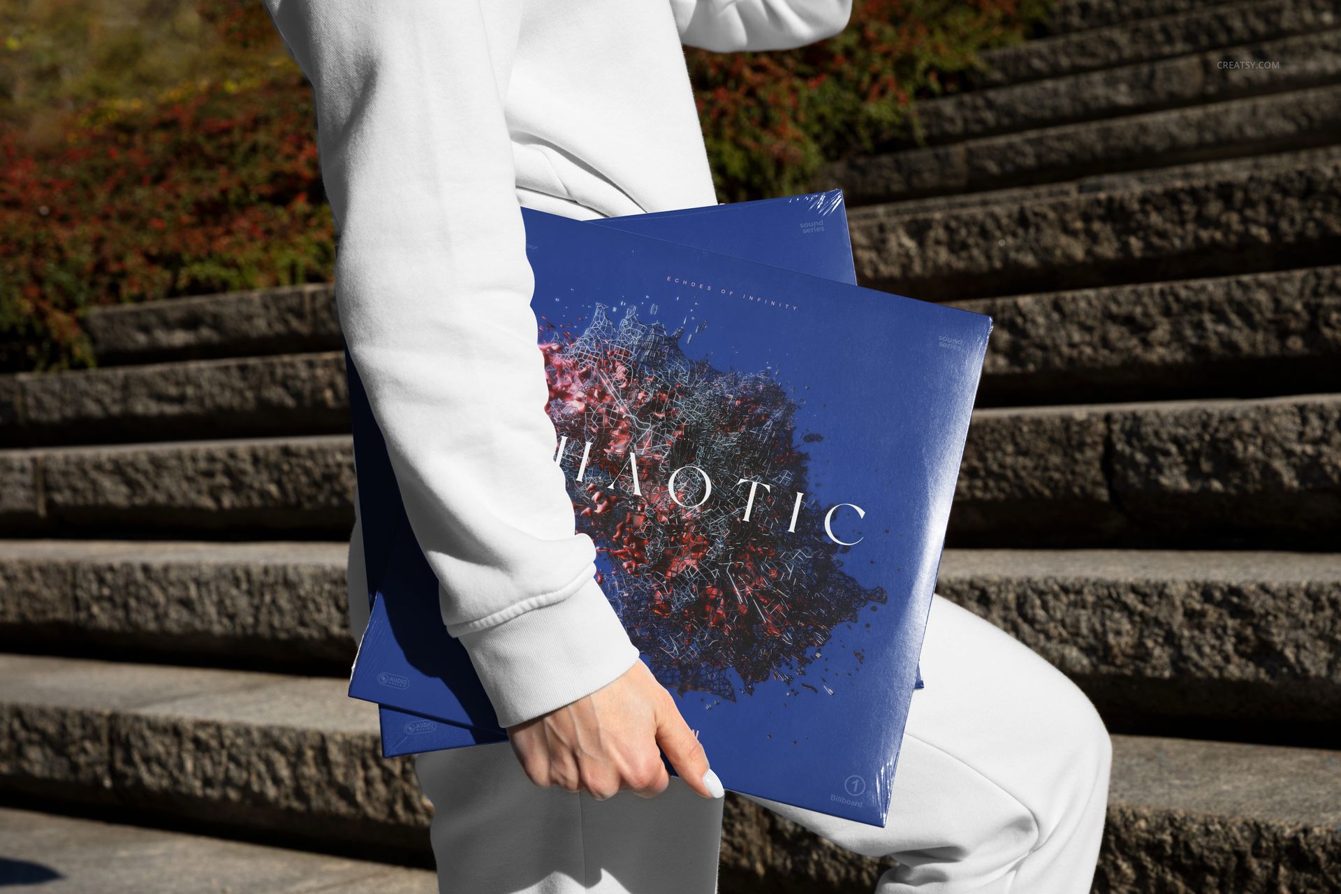 Outdoor scene featuring a person in light attire holding two colored vinyl record mockup covers with artistic patterns.