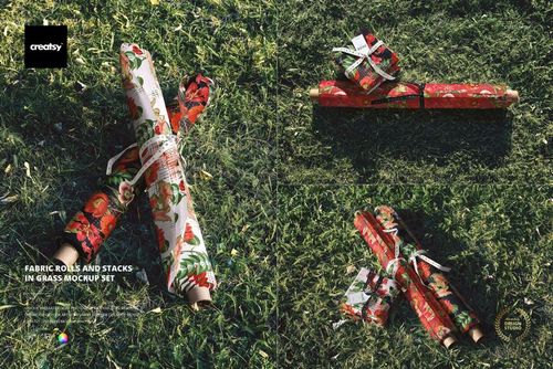 PSD mockup showing patterned fabric rolls and stacks with red and white designs lying on sunlit grass.
