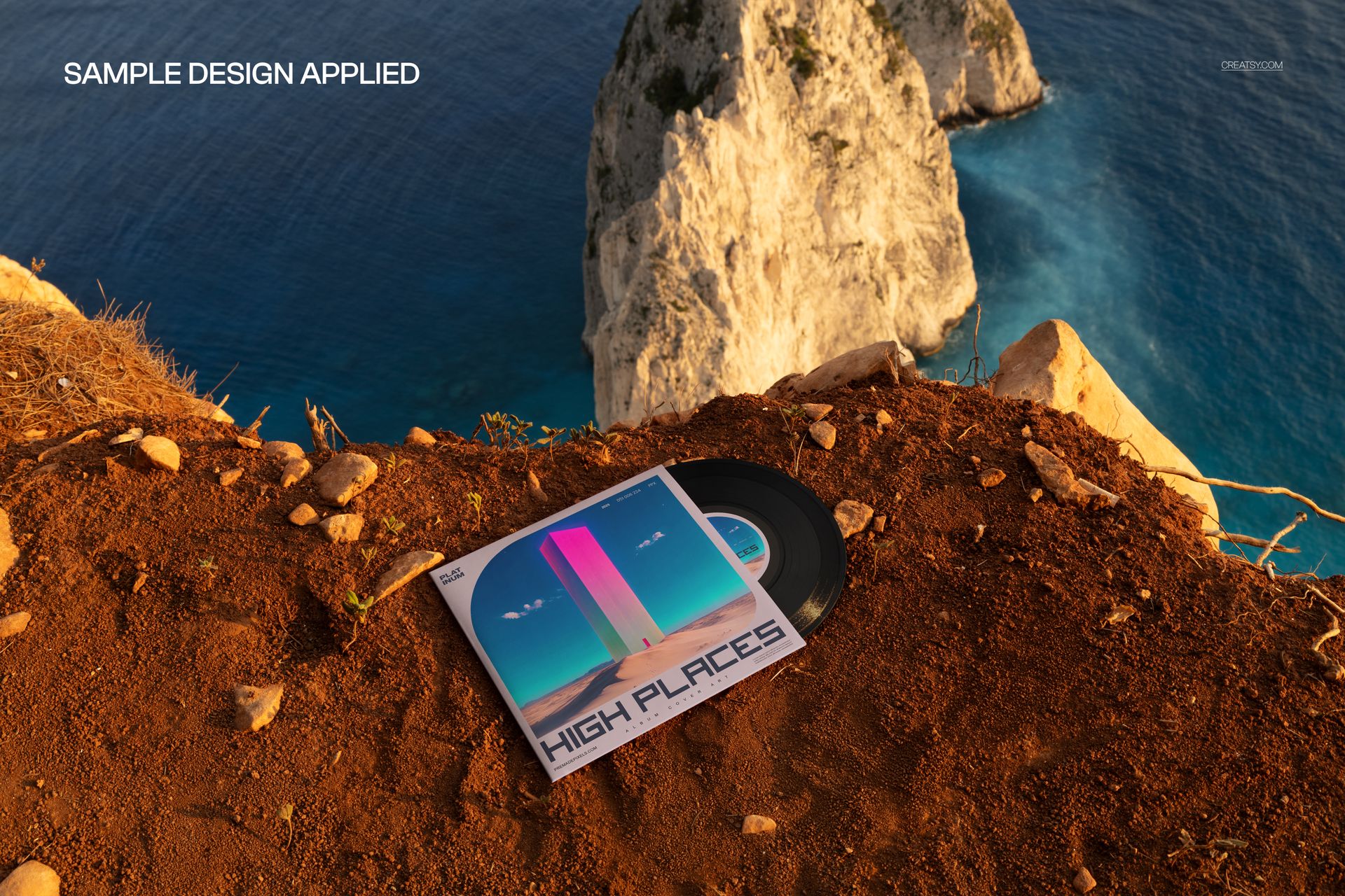 Black vinyl record and square album cover mockup on rocky ground overlooking blue sea and white cliffs, high angle view.