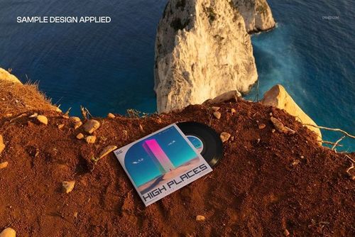 Black vinyl record and square album cover mockup on rocky ground overlooking blue sea and white cliffs, high angle view.