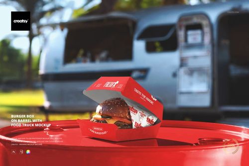 Open burger box mockup on a red barrel, displaying a burger with lettuce and tomato, with a food truck in background.