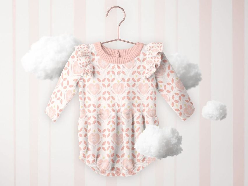Hanging knitted romper mockup featuring a pink and white floral pattern, surrounded by fluffy clouds on a striped background.