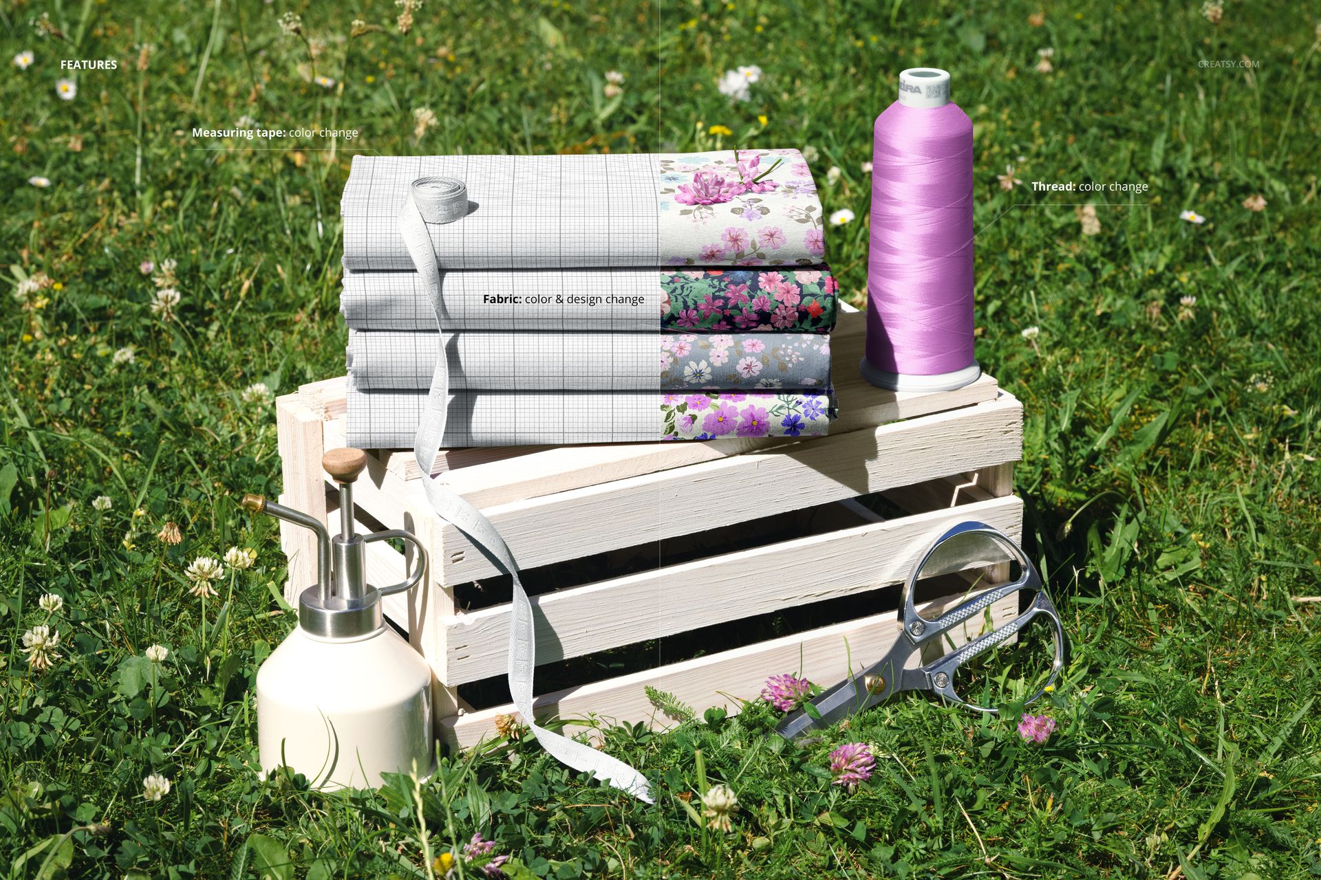 Outdoor scene featuring a PSD mockup of jersey fabric stack with floral prints, thread spool, and scissors on grass.