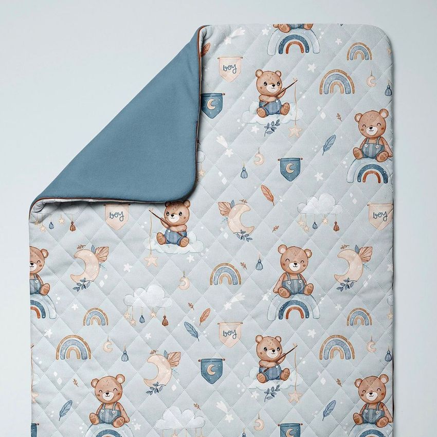 Double-sided baby bedding set mockup featuring a quilted blanket with a boho bear and rainbow pattern on a light background, shown from above.