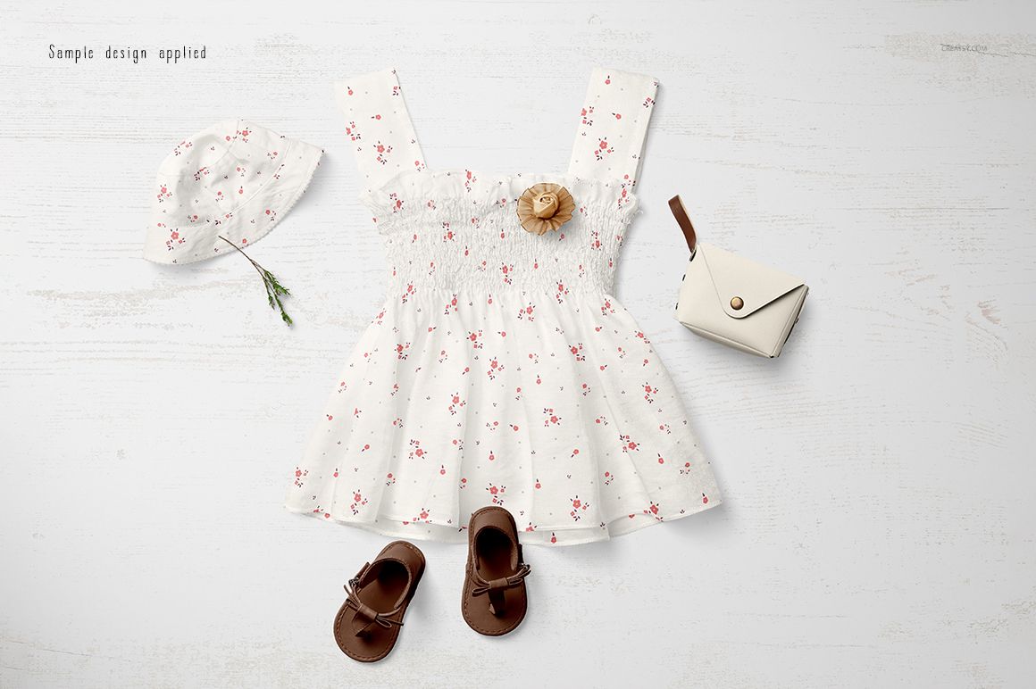 Baby summer set mockup featuring a white dress with small floral pattern, matching hat, sandals, and small purse on a light surface.