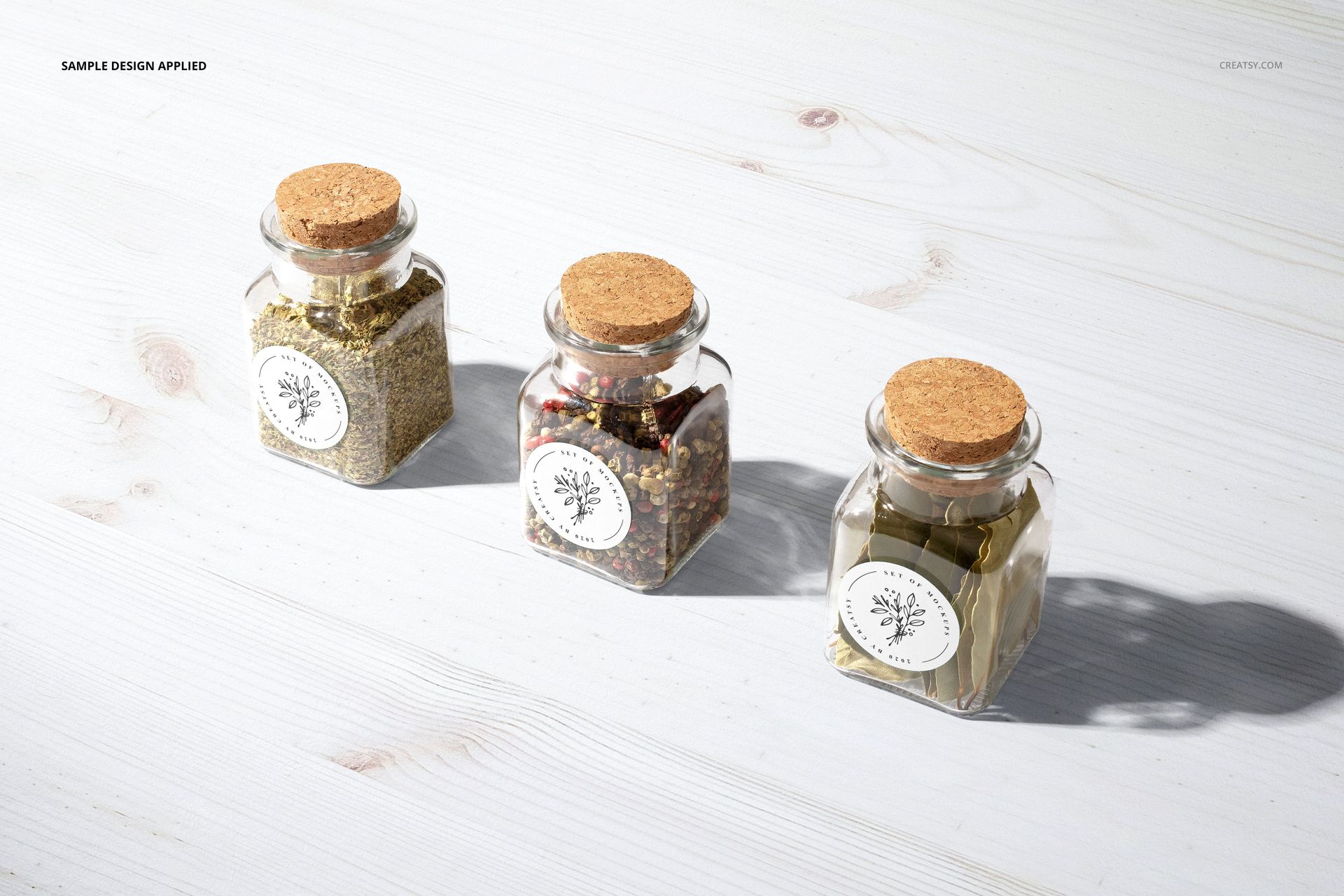 Spice jar PSD mockup featuring three clear jars with cork lids and round white labels, placed side by side on wood.