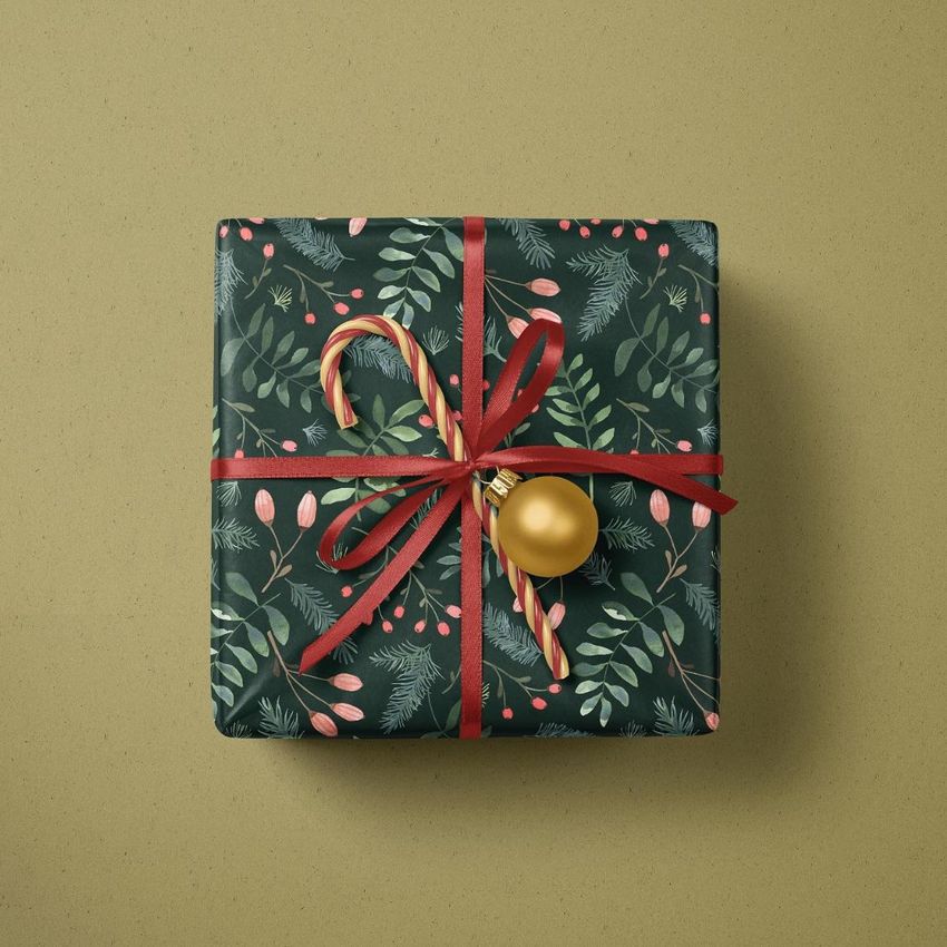 Christmas gift mockup featuring a box wrapped in green festive paper with red ribbon, topped with a candy cane and gold ornament.