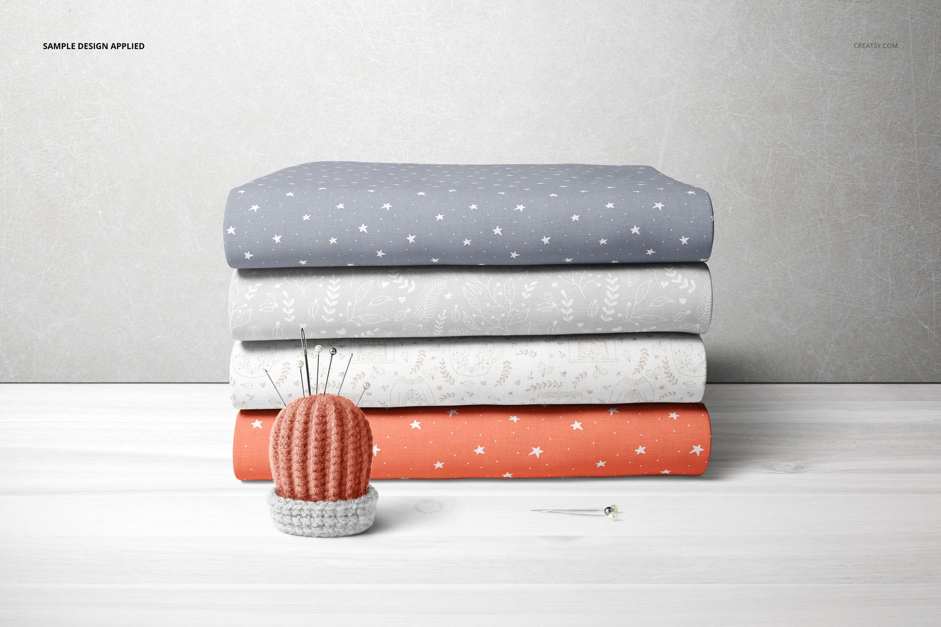 Folded fabric stack mockup with blue, gray, and coral textiles displaying small stars and foliage designs, front perspective.