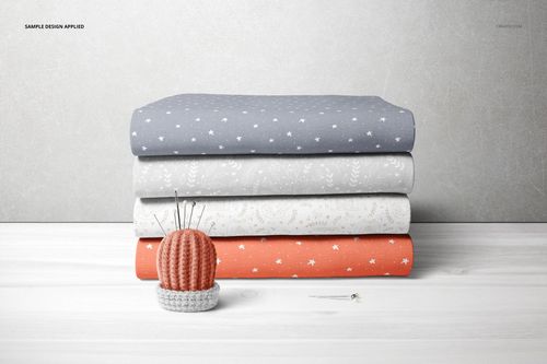 Folded fabric stack mockup with blue, gray, and coral textiles displaying small stars and foliage designs, front perspective.