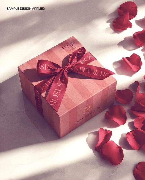 PSD mockup of a square gift box with a bow, pink stripes, and rose petals arranged around it on a bright background.