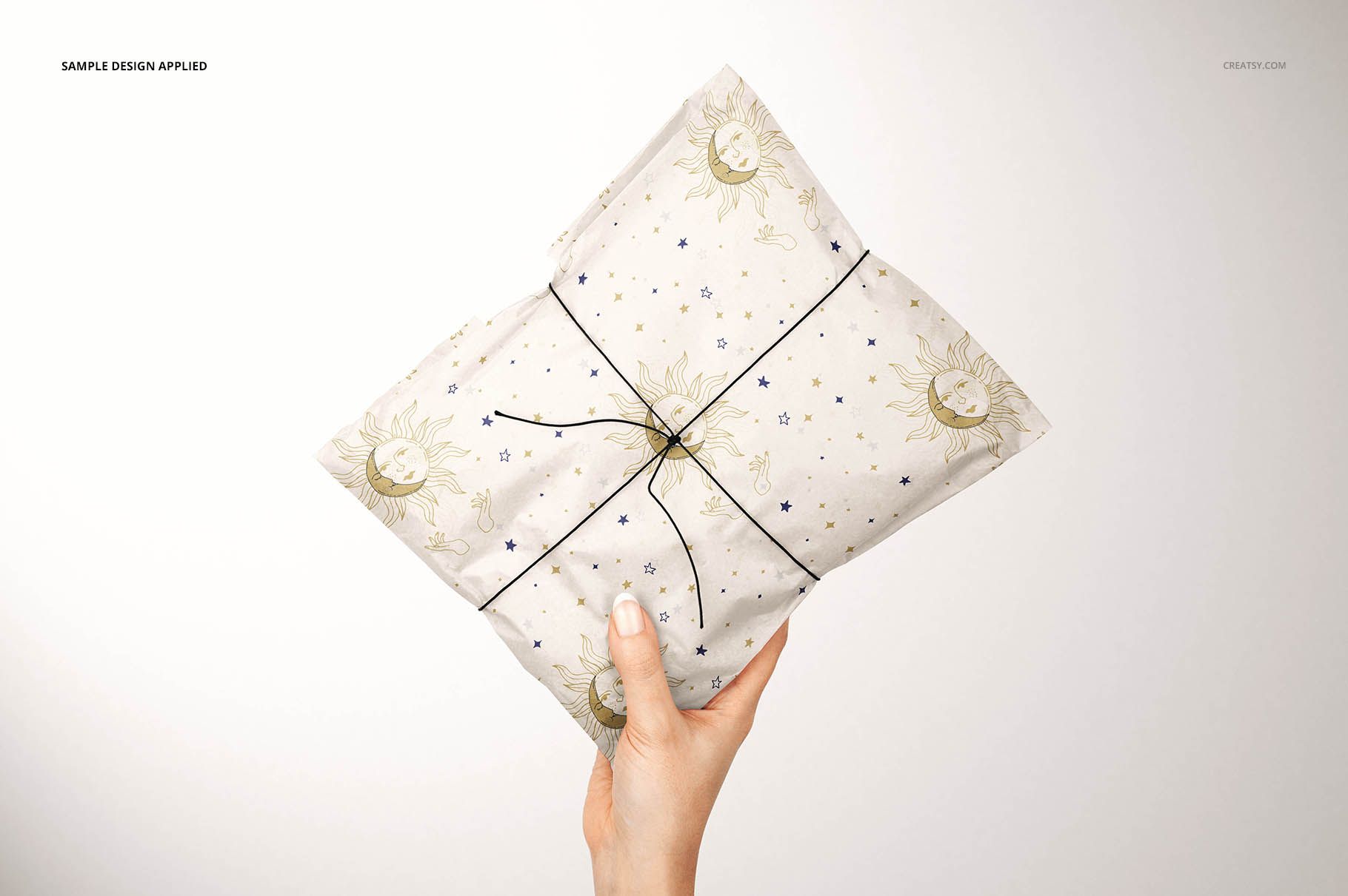 Mockup of a gift package covered in white tissue paper with gold sun and blue star pattern, held against a plain background.