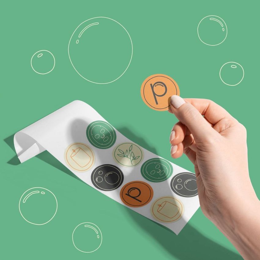 Round sticker mockup featuring a hand picking up a label from a sheet, with simple icon designs and a playful green background.