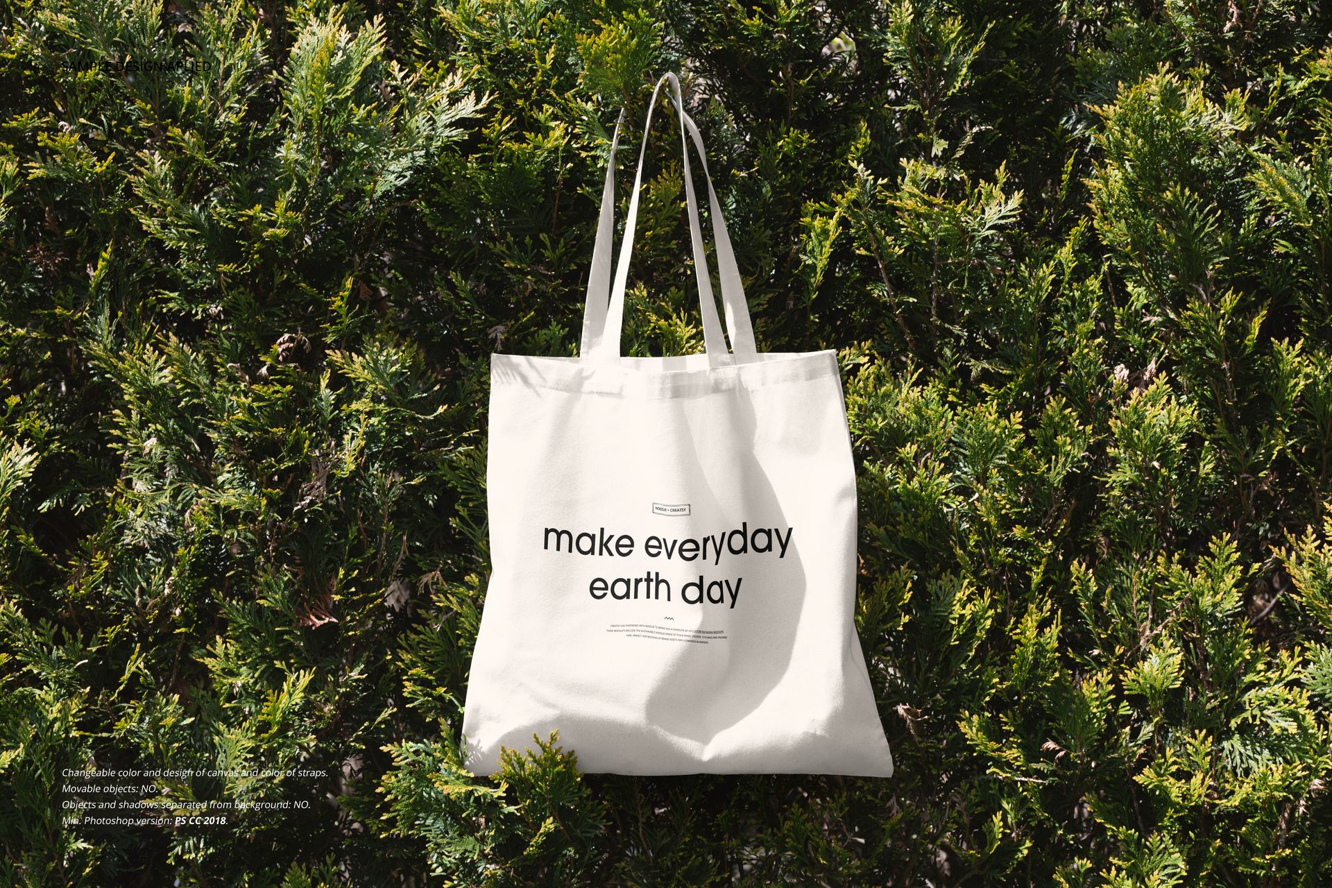 Noissue tote bag mockup showing a white fabric bag with black lettering, hanging on lush outdoor shrubbery.