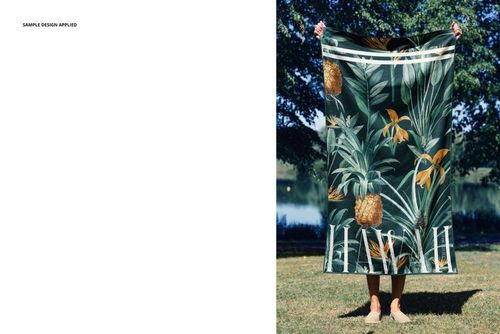 Front view of a beach towel mockup featuring a vibrant tropical design with pineapples and leaves in a park setting.