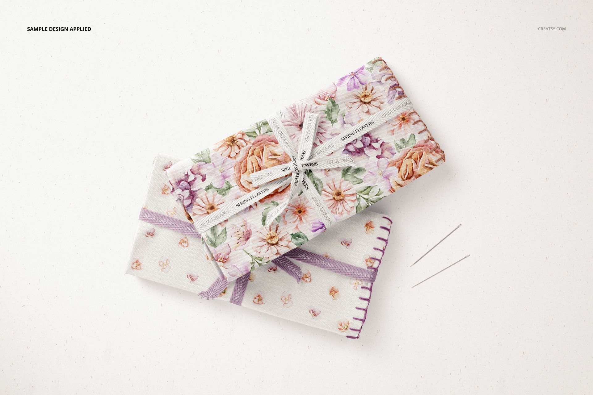 Folded fabric mockup set showing floral textiles, ribbons, and needles from a top perspective on a neutral surface.
