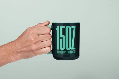 PSD mockup of a 15oz mug in dark color, featuring prominent turquoise text and a hand gripping the handle.