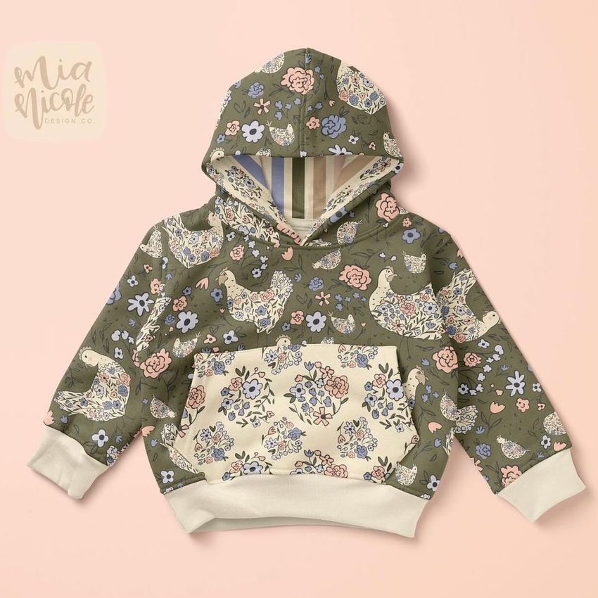 Kids hoodie mockup featuring a floral hen pattern in muted green, pink, and blue tones on a light pink background.