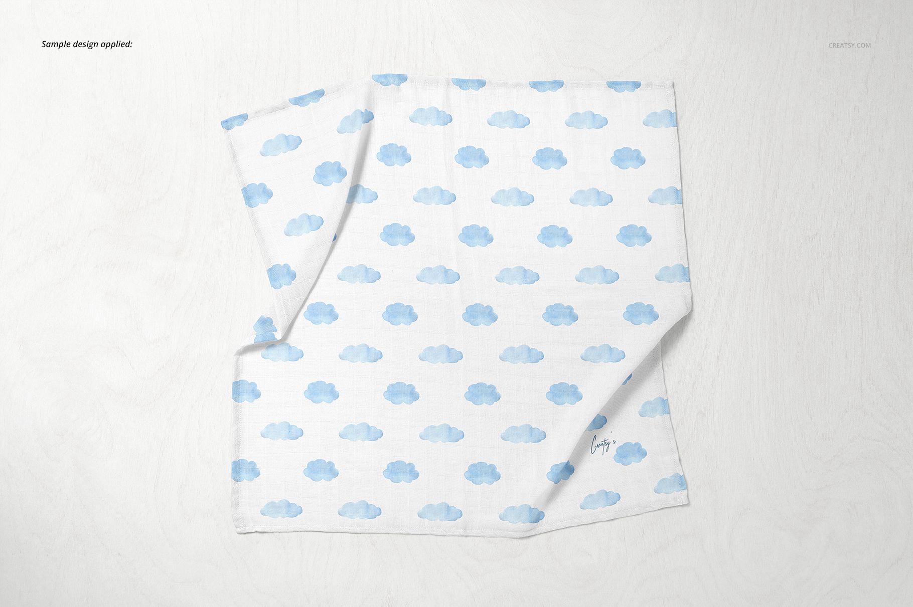 Baby muslin square nappy mockup featuring a blue cloud design, laid out flat on a pale wood background.
