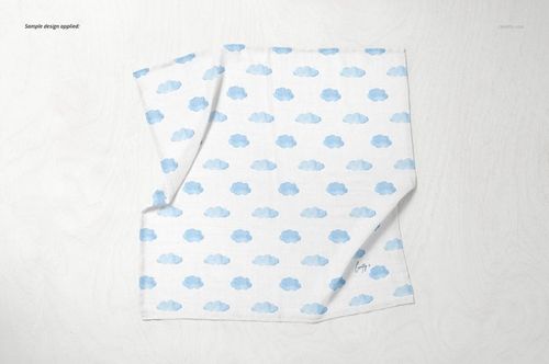 Baby muslin square nappy mockup featuring a blue cloud design, laid out flat on a pale wood background.
