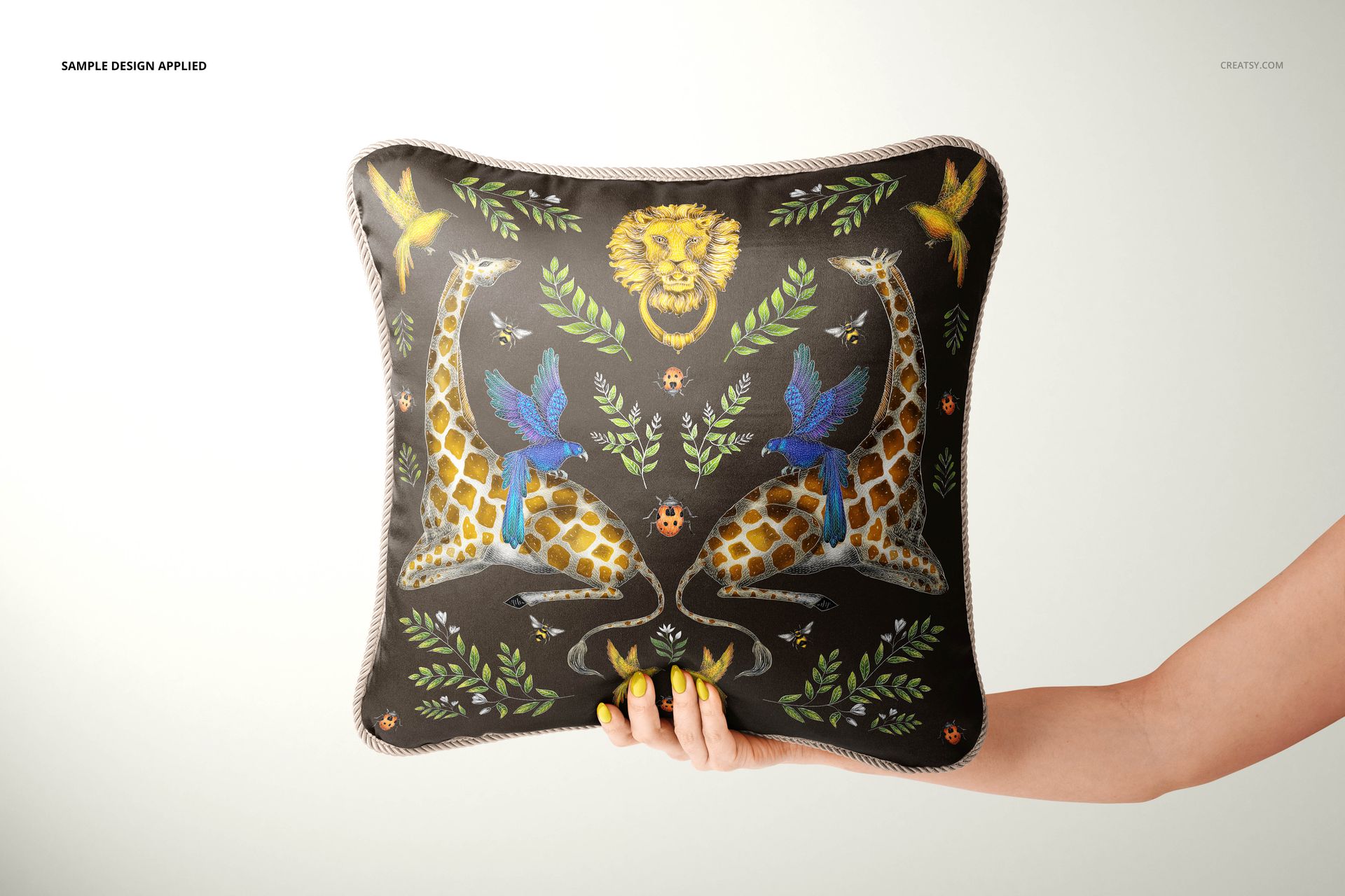 Front view of a silk cushion mockup with braided trim, decorated with giraffes, leaves, and animal motifs on dark fabric.