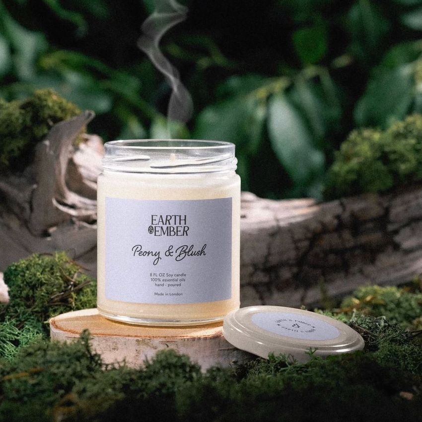 Scented soy candle mockup featuring a glass jar with a white label, placed on mossy ground with a wooden lid nearby.