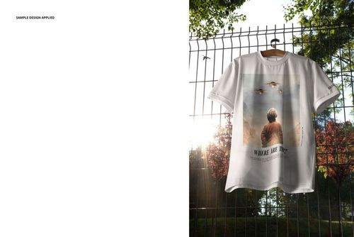 Front view of an oversized t-shirt mockup with a graphic design, displayed on a hanger against a wire fence and trees.