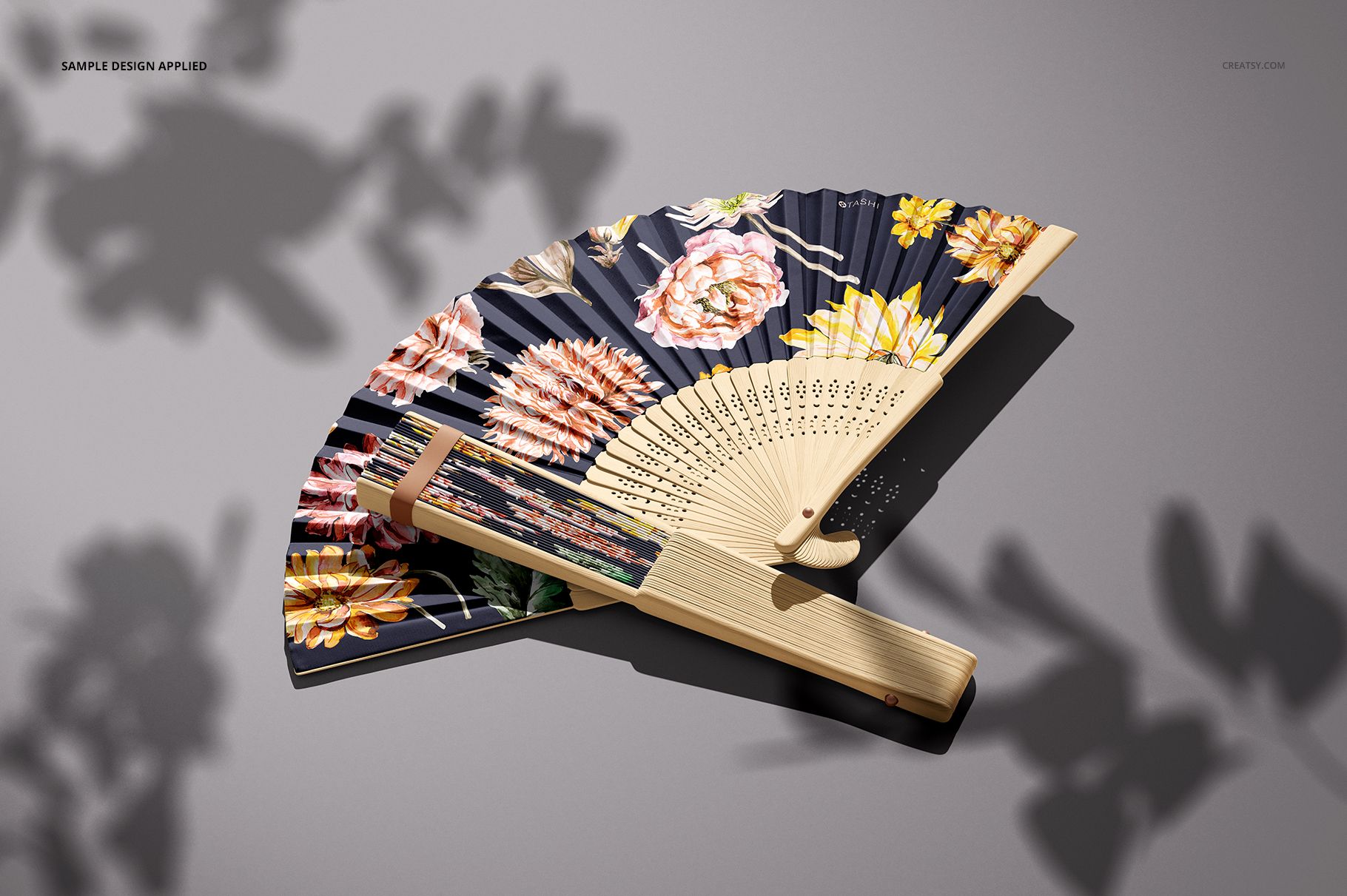 PSD mockup of a fabric hand fan with light wood ribs and a navy background decorated with colorful flowers.
