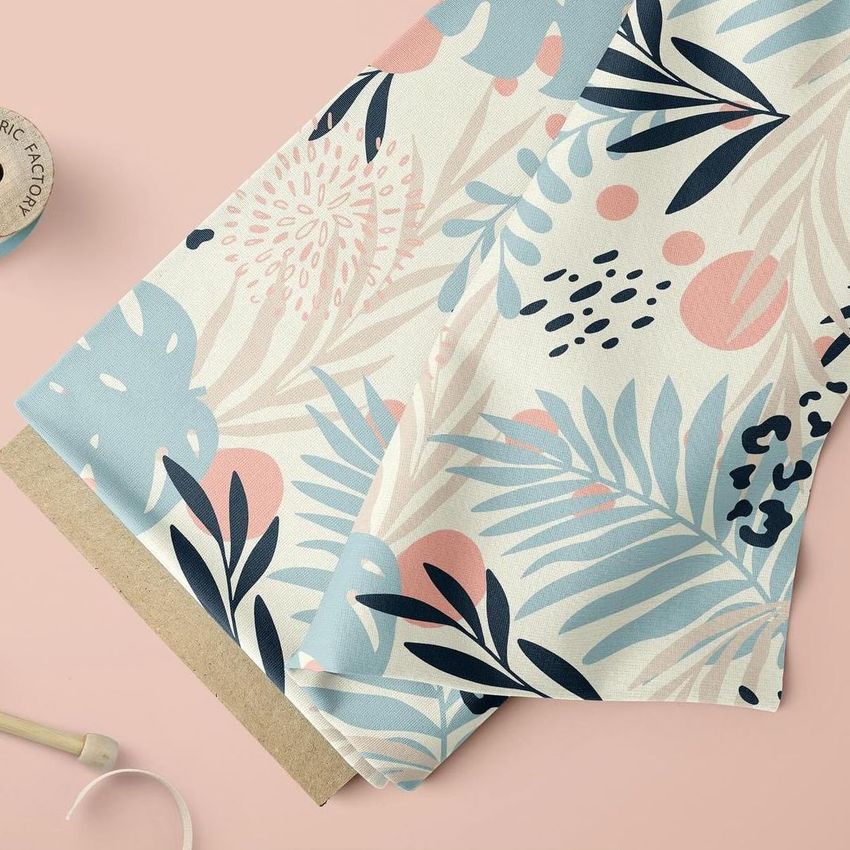 Fabric mockup showing a close-up of a folded bolt with a tropical floral pattern in blue, pink, and beige on a light surface.