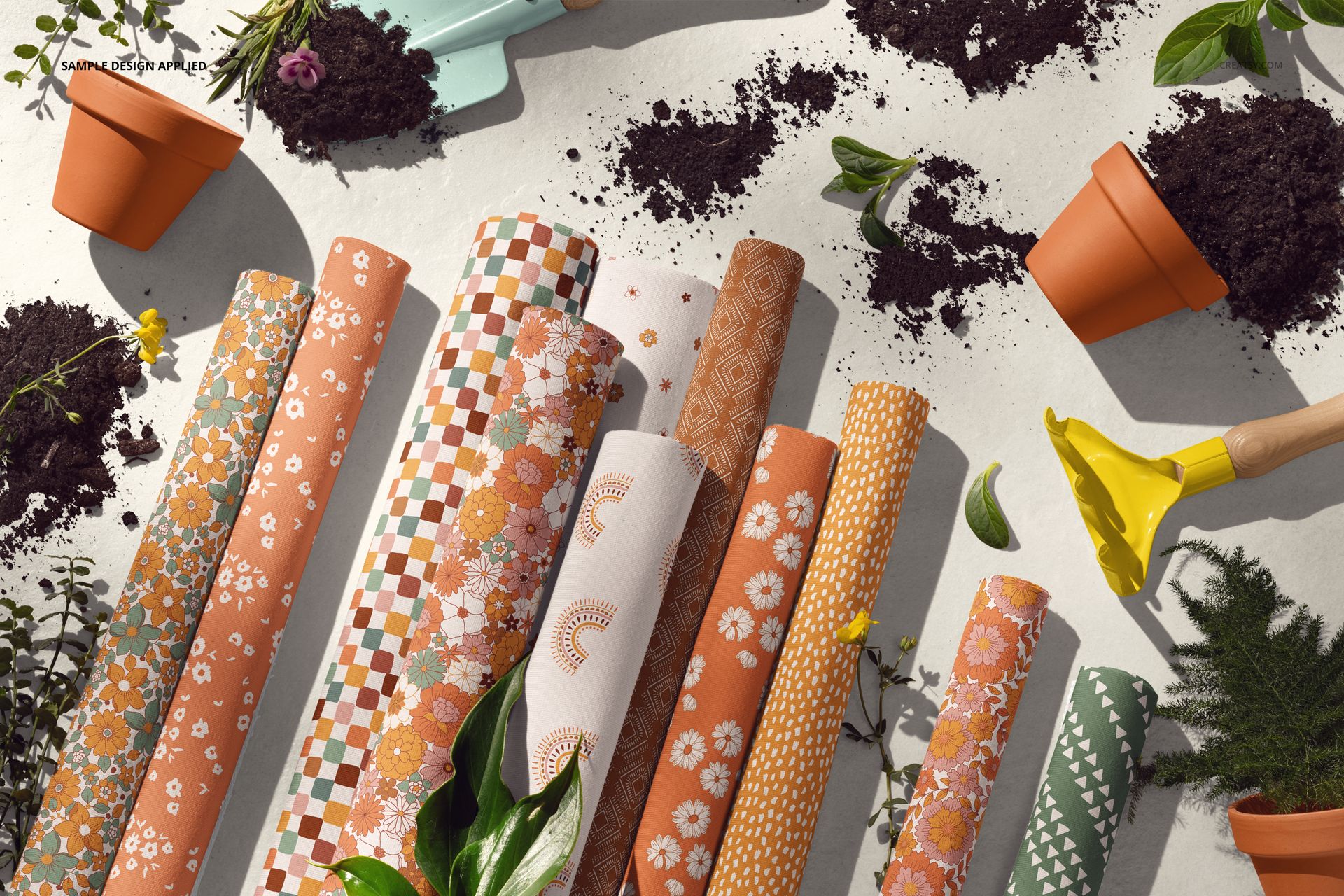 PSD mockup showing several patterned jersey fabric rolls in a garden-themed scene with scattered soil and gardening props.