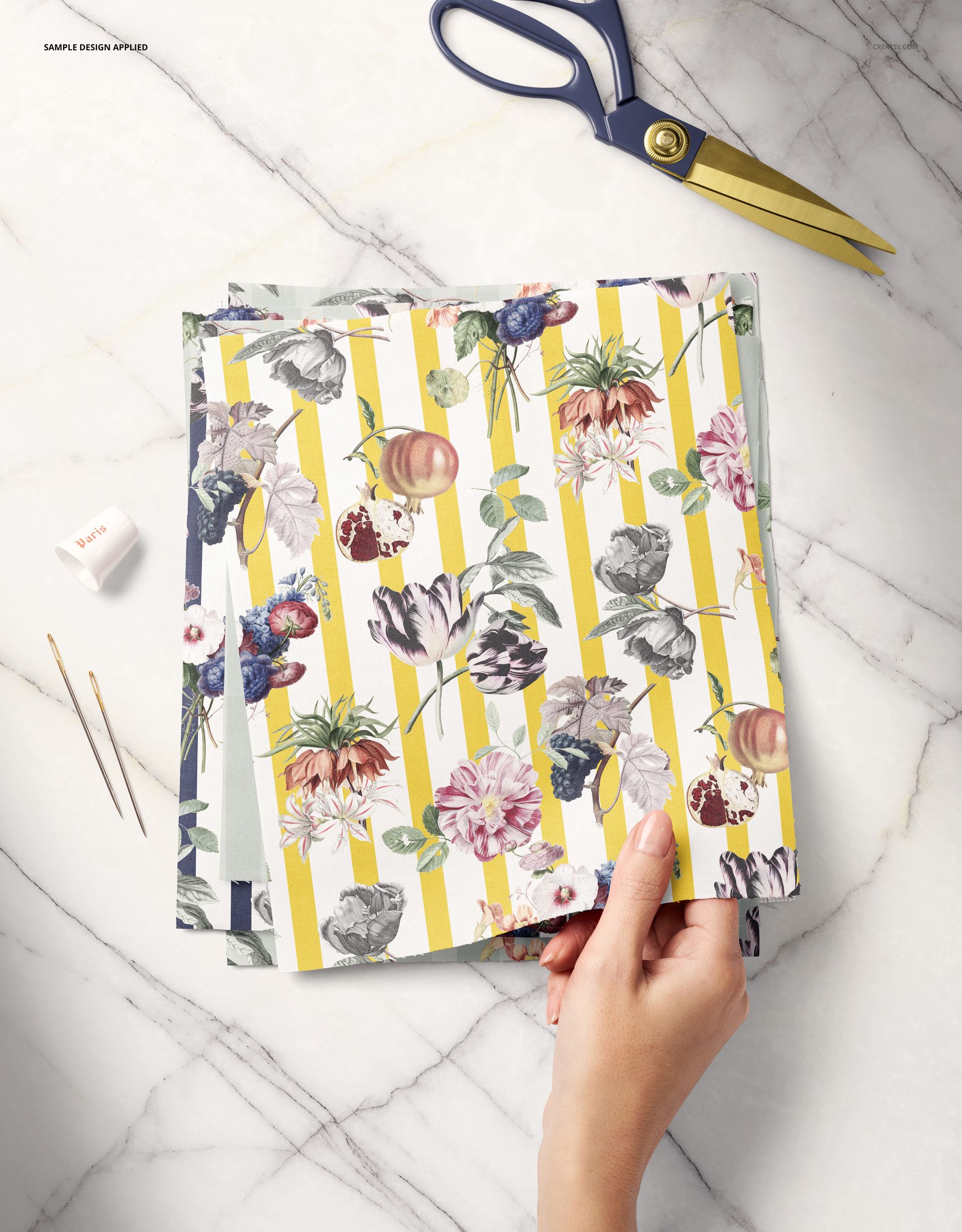 PSD mockup featuring fabric swatches with colorful floral prints and stripes, hand and sewing accessories visible on table.