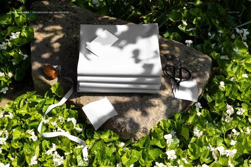 PSD mockup showing folded fabrics on a textured rock outdoors, with scissors, tape measure, and leafy plants nearby.