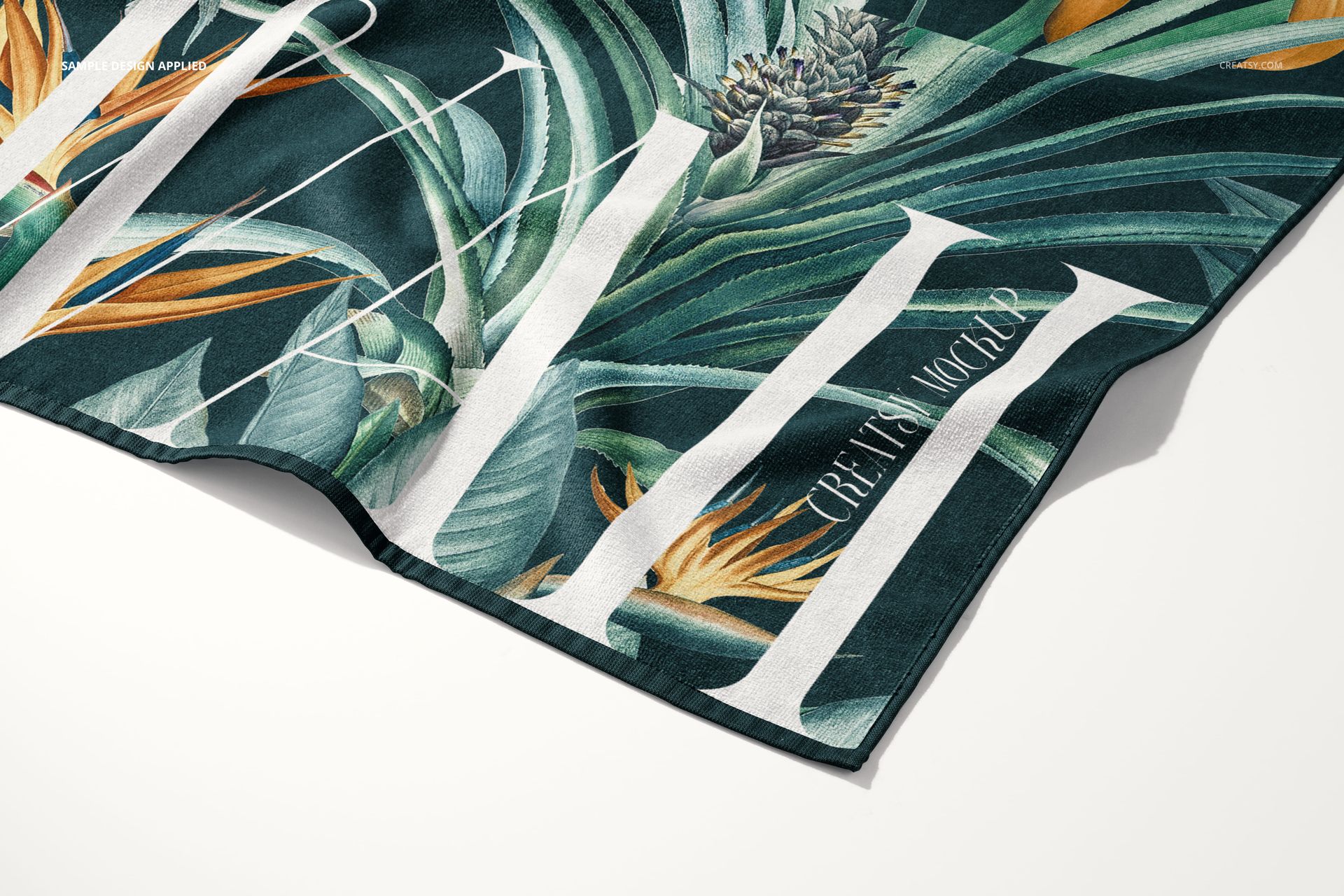 Beach towel mockup featuring a close-up of a corner with tropical leaf and flower pattern in green and orange tones.