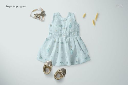 PSD mockup showing a soft blue baby dress with whimsical designs, arranged alongside gold shoes and decorative props.