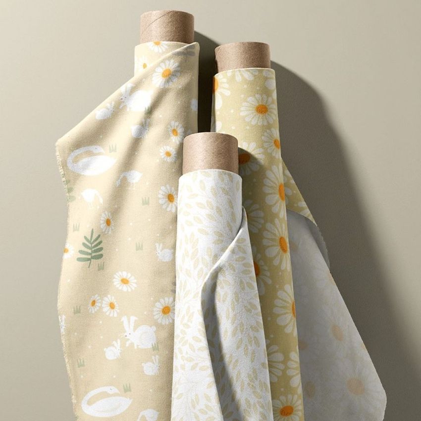 Fabric rolls mockup showing three upright rolls with pastel yellow and white daisy and animal patterns on a neutral background.