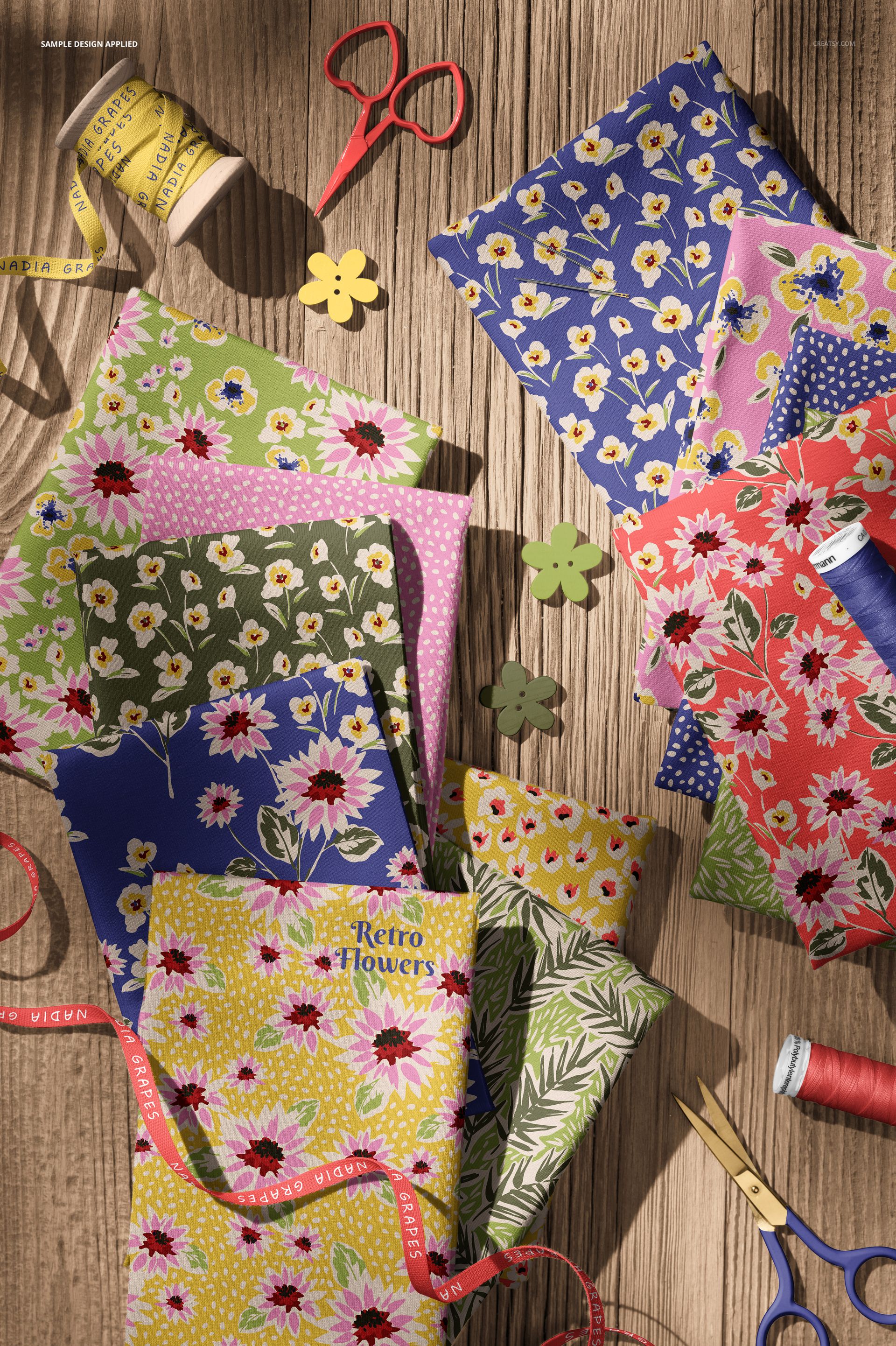 PSD mockup showing multiple flower-patterned jersey fabric pieces and sewing accessories in a flat lay composition.