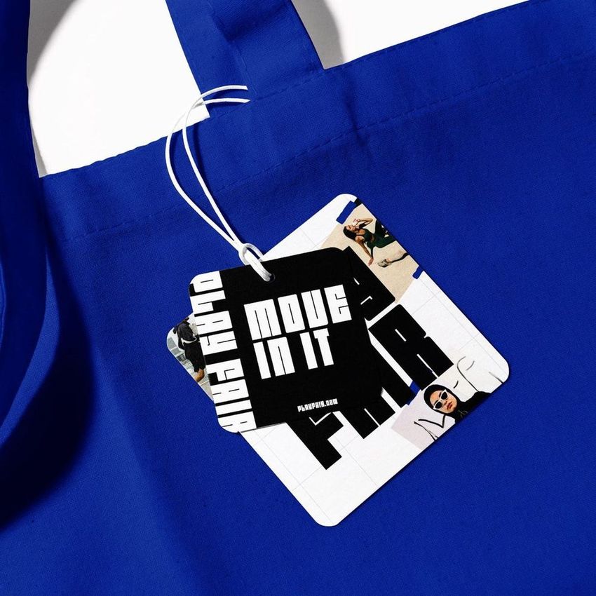 Canvas tote bag mockup in vivid blue fabric, shown close-up with attached square tag featuring bold text and photo collage.